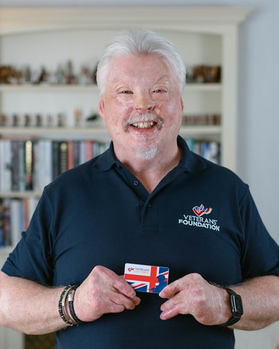 Simon Weston smiling, holding a Veterans' Lottery card
